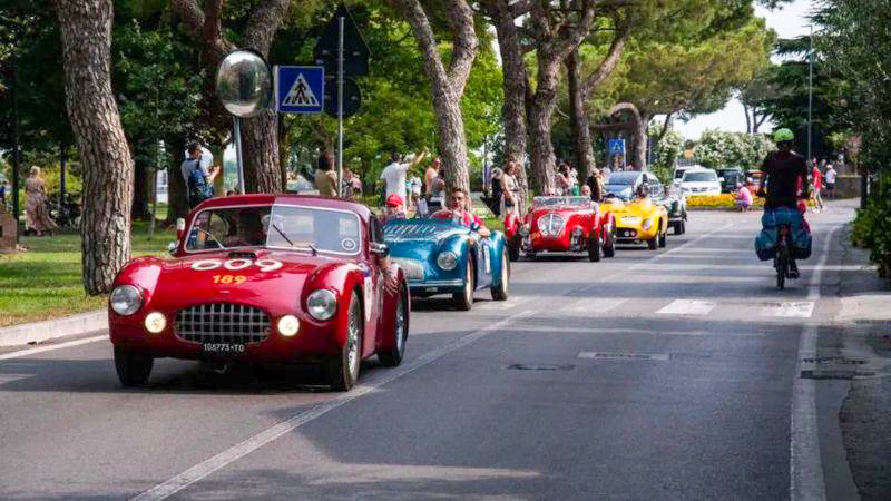Vintage red Mille Miglia barchetta number 189 leading a small group along a tree-lined Italian street