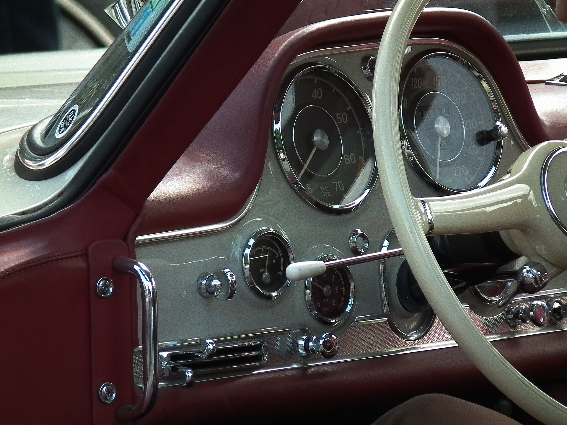 The interior of a Mercedes-Benz 300 SL, showing the plaid seats, white steering wheel, and classic dashboard.